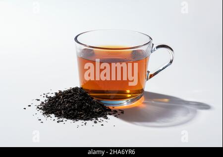 Thé chaud et feuilles de thé dans un verre sur fond blanc Banque D'Images