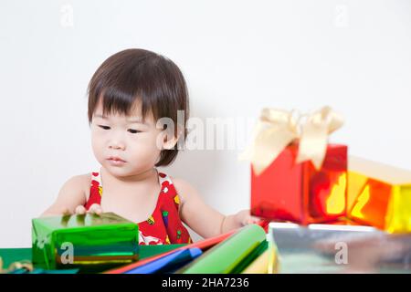 Adorable petite fille asiatique intéressant emballer une belle boîte cadeau sur table, sur fond blanc Banque D'Images