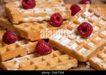 Un bouquet de gaufres belges saupoudrées de sucre et de framboises, sur un papier de cuisson sur un fond rustique en bois Banque D'Images