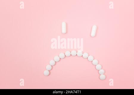 Préjudice pharmaceutique. Sad Smiley visage fait de pilules blanches, couché sur le Backgrond rose. Industrie pharmaceutique mondiale et médicaments Banque D'Images