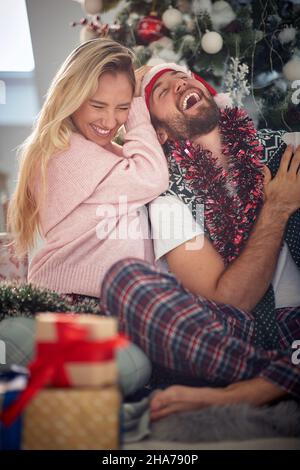 Un gars a un bon moment avec sa petite amie pendant qu'ils sont assis sur le sol pendant les vacances de noël dans une atmosphère gaie à la maison togethe Banque D'Images