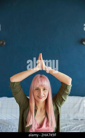 La femme aux cheveux longs tient les mains dans la mudra namaste au-dessus de la tête dans la chambre à coucher Banque D'Images