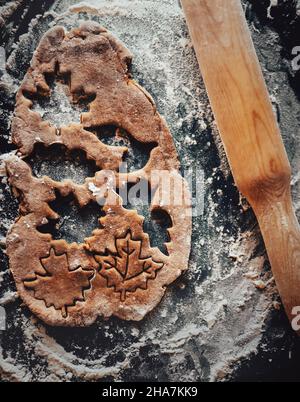 Vue de dessus de la pâte dans laquelle les chiffres de pain d'épice sont coupés.La pâte repose sur une plaque de cuisson saupoudrée de farine, et il y a une broche de roulement à côté Banque D'Images