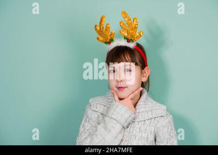 Studio portrait d'une enfant fille pensive portant des cornes de cerfs jaunes isolées sur fond de menthe Banque D'Images