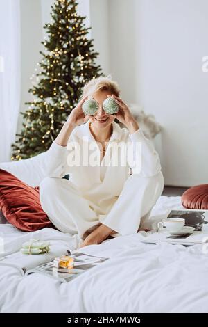 Jeune belle femme dans un intérieur moderne du nouvel an, dans une chambre blanche, sur le fond des lumières de bokeh d'un arbre de Noël avec décoration Banque D'Images