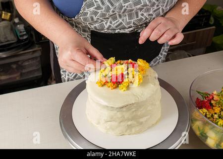 Pâtisserie décorant un gâteau avec une ganache au chocolat blanc et des fleurs jaunes. Banque D'Images