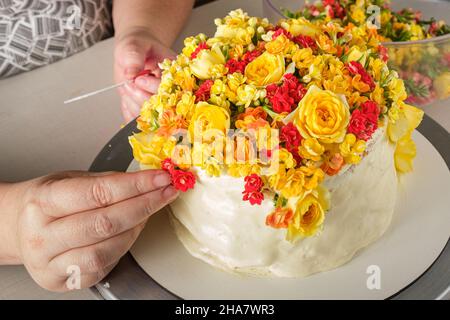 Confiseur décorant un gâteau à la vanille avec des fleurs jaunes et rouges. Banque D'Images