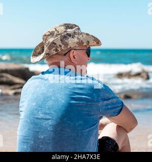 un homme âgé s'assoit sur la mer par une belle journée d'été et regarde au loin Banque D'Images