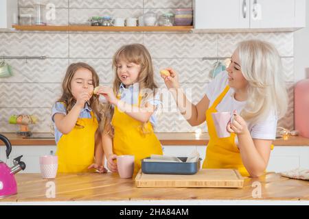 Les filles d'enseignement de maman caucasienne souriante goûtent les biscuits juste cuits ensemble dans la cuisine.Concept de cuisine maison Banque D'Images