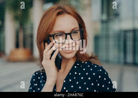 Belle femme rouge a la conversation téléphonique utilise un smartphone pour les appels Banque D'Images