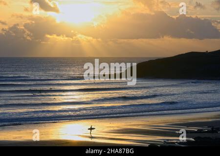 Un surfeur silhoueté dans le soleil couchant se reflète dans le sable humide et surf au bord de l'océan Banque D'Images