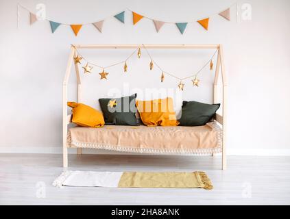 Chambre élégante pour enfants avec lit Montessori décorée de coussins de couleur couchée, drapeaux en papier et étoiles dorées accrochées à la corde pour rehausser le gaifu Banque D'Images