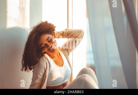 Heureuse fille afro-américaine d'origine ethnique dans la maison assise sur le rebord de fenêtre sur toile de fond de rideaux flottant du vent léger, Happy afro Banque D'Images