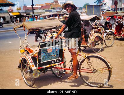 1970S CHAUFFEUR DE TAXI SOURIANT DE PEDIAB BENCHER À JAKARTA JAVA INDONÉSIE - DÉSORMAIS INTERDIT DE LA VILLE POUR CAUSE DE CONGESTION DE LA CIRCULATION -KR25601 SPE001 HARS INDONÉSIE HOMMES VÉLOS TRANSPORT VÉLOS OEIL CONTACT COMPÉTENCES MÉTIER GAI AVENTURE SERVICE À LA CLIENTÈLE SONT DES OCCUPATIONS DE FIERTÉSOURIT LES VILLES CAPITALES DE L'ASIE DU SUD-EST JAKARTA JOYEUSE JAVANAIS CAUSANT LA CONGESTION JAVA OCÉANIE PÉDICAB VIEUX MODE Banque D'Images