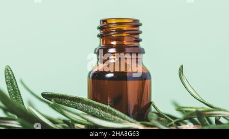 Huile essentielle de romarin dans une bouteille ouverte brune à côté des herbes fraîches sur fond vert, gros plan Banque D'Images