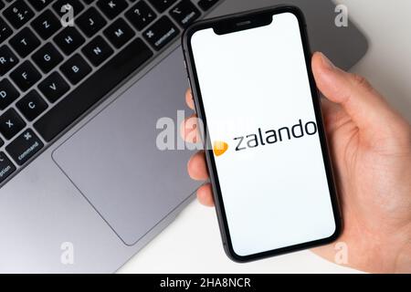 Zalando application sur l'écran de smartphone dans la main des mans avec un ordinateur portable sur l'arrière-plan.Achats en ligne par téléphone portable.Novembre 2021, San Francisco, États-Unis Banque D'Images