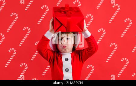 Enfant de Noël avec cadeau.Aide pour le père Noël avec boîte cadeau.Enfant garçon en costume de père Noël.Publicité de la nouvelle année Banque D'Images