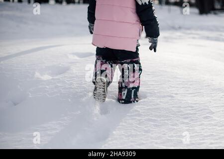 L'enfant marche à travers la chasse-neige.Vue arrière de la petite fille en veste d'hiver rose marchant le long de la route enneigée dans le parc après de fortes chutes de neige sous le soleil givré Banque D'Images