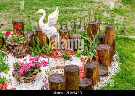 Aménagement de jardin avec des rondins en bois, paniers en osier, gravier et ornement en forme de cigognes Banque D'Images