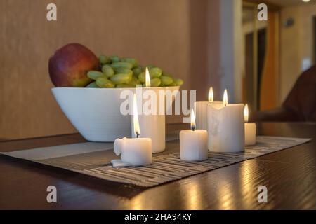 bougies allumées et vase avec pommes de fruits et raisins sur la table près de la lampe Banque D'Images