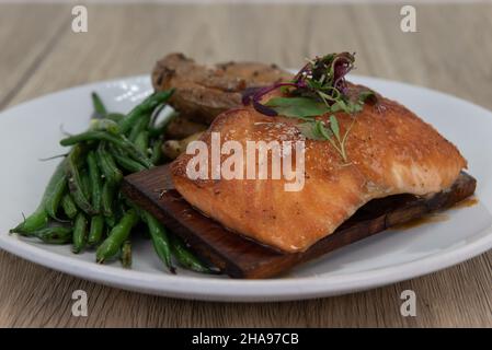 Présentation artistique du saumon en bois de cèdre grillé avec une surface croustillante et servi avec des haricots verts et des pommes de terre cuites au four. Banque D'Images