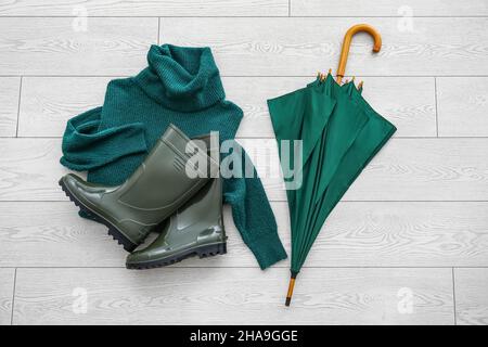 Parapluie, chandail et bottes en caoutchouc sur fond de bois clair Banque D'Images