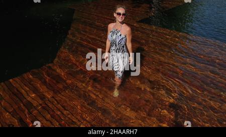 Femme marche sur l'eau sur l'embarcadère de lunettes de soleil et un châle en soie boho. Girl reste sur des zones sous-marines bois dock. Le trottoir est couvert avec de l'eau dans le lac. Banque D'Images