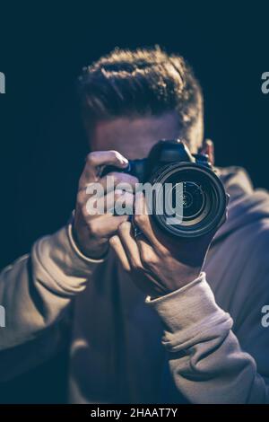 Un homme photographe avec un appareil photo prend une photo dans l'obscurité. Banque D'Images