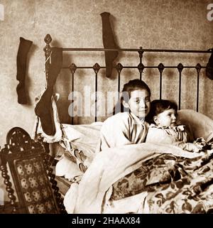 Enfants avec leurs bas sur leur lit pour des cadeaux le réveillon de Noël, période victorienne Banque D'Images