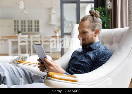 Souriant gadget utilisateur homme lisant le livre sur l'écran de l'ordinateur tablette Banque D'Images