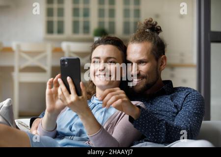 Joyeux couple millénaire joyeux prenant le selfie sur le canapé à la maison Banque D'Images