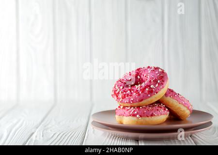 Beignets à la glaçure rose et à la poudre de caramel colorée sur fond blanc en bois. Banque D'Images