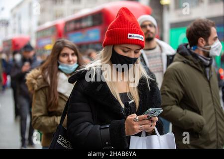 Londres, Royaume-Uni.11th décembre 2021.Un acheteur portant un masque facial comme mesure préventive contre la propagation du covid-19 a vu communiquer sur un téléphone mobile tout en marchant le long d'Oxford Circus à Londres.Crédit : SOPA Images Limited/Alamy Live News Banque D'Images