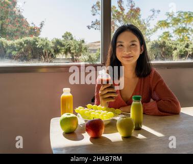 jeune femme posant assise avec une table pleine de fruits et smoothies, paysage naturel en arrière-plan Banque D'Images