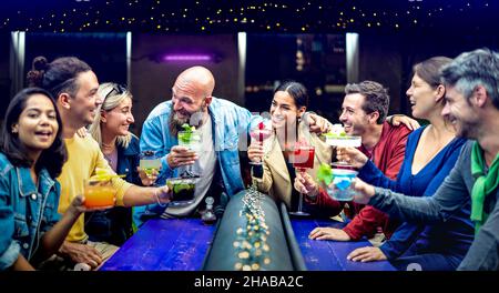 Des gens multiculturels dégustent des boissons de fantaisie multicolores au bar de la mode - des jeunes amis s'amusent ensemble à boire un cocktail à l'happy hour Banque D'Images