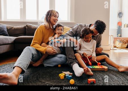 Les jeunes parents jouent avec leur fils et leur fille dans la salle de séjour.Maman et papa s'amusent avec leurs enfants pendant les heures de jeu.Famille de quatre personnes dépensées Banque D'Images