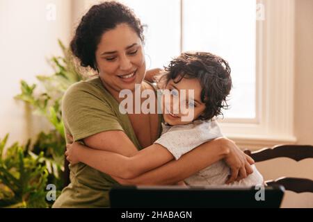 Mère de soutien embrassant son fils tout en regardant un tutoriel en ligne.Mère et fils sourient en regardant une tablette numérique.Amour simple Banque D'Images