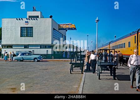 Une scène animée à la gare de Las Vegas, Nevada USA en 1956 – un train Union Pacific est arrivé à la plate-forme.La gare ferroviaire de style «Treamline moderne» a été construite en 1940 et améliorée avec des lumières au néon en 1946 (notez le signe distinctif au néon en forme de moteur de chemin de fer jaune sur le bâtiment).La gare desservait plusieurs trains Union Pacific par jour, reliant Los Angeles à l'ouest et Salt Lake City, puis Chicago et St. Louis à l'est.Cette station a été démolie en 1971 – une photographie vintage de 1950s. Banque D'Images