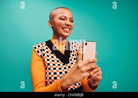 Prendre un selfie mignon.Une jeune femme heureuse souriant avec ses yeux fermés tout en capturant un autoportrait sur son smartphone.Femme aux cheveux courts debout Banque D'Images