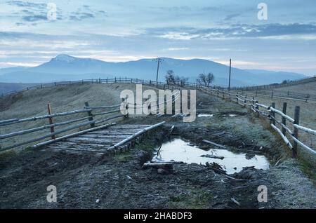 Paysage du matin avec route rurale et flaques.Givre sur le sol et clôture dans un village de montagne.Carpates, Ukraine, Europe Banque D'Images