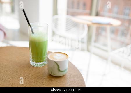 Cappuccino et thé vert glacé matcha latte dans une tasse en céramique sur une table en bois dans un café de style moderne.Boissons savoureuses le matin. Banque D'Images