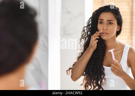 Épilation de la lèvre supérieure.Femme frustrée avec Razor en main regardant le miroir Banque D'Images