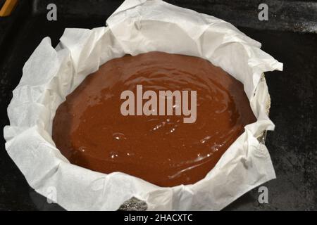 Pâte au chocolat dans un moule de cuisson en aluminium rond fait maison recouvert de papier blanc pour cuire une tortilla à gâteau sur fond noir. Banque D'Images