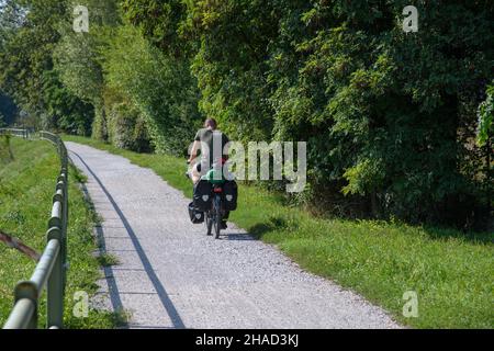 Un cycliste unique avec un vieux vélo et des valises sur une piste cyclable poussiéreuse et non pavée. Banque D'Images