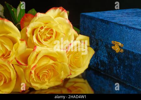Un bouquet de roses, jaune avec une bordure rouge et une boîte cadeau en velours bleu, fermée par une serrure dorée. Banque D'Images
