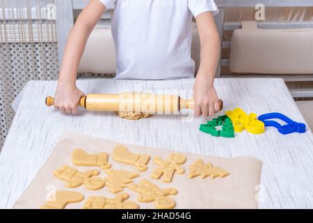 Noël et la tradition du nouvel an.L'enfant roule la pâte avec une broche sur la table dans la cuisine.Coupé à partir de la forme de pâte brute d'un Christm Banque D'Images
