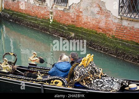 Un couple est assis dans une gondole sur un canal de Venise et admire la ville. Banque D'Images