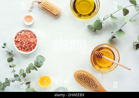 Ingrédients naturels pour un gommage maison.Huile, miel, sel himalayan rose, brosse pour le visage ou le corps, branches de citron et d'eucalyptus sur table blanche en bois.Haut Banque D'Images