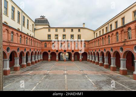 La cour à arcades rouge et blanche de l'ancien couvent des Minimes se trouve vide au centre de l'actuel complexe de la mairie de Saint-Chamond, dans le département de la Loire, en France. Deux étages avec des fenêtres en arc rond entourent la cour sur trois côtés, et une petite lanterne avec une girouette couronne le faîtage du bâtiment arrière. La cour mène au Parc Nelson Mandela, l'ancien jardin du couvent. Banque D'Images