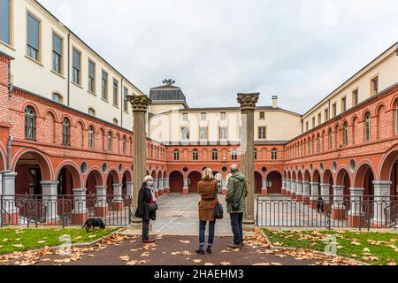 Sylvia Kuhn-Heusler (à gauche) avec son chien, Angela Berg (au centre) et Michel Bezacier (à droite) se tiennent entre deux colonnes corinthiennes dans la cour à arcades de l'ancien couvent des Minimes du Parc Nelson Mandela à Saint-Chamond, dans le département de la Loire, en France. Ils regardent vers le bâtiment de la mairie centrale à l'autre bout de la cour, des feuilles d'automne recouvrent la pelouse à leurs pieds. Banque D'Images